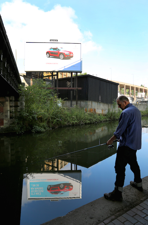 Man_Goes_Fishing_under_Spaghetti_Junction,_Birmingham_with_Car_Advert_(portrait)_ref_P5362